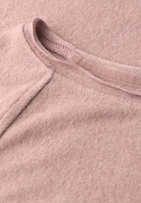 Helles rosa Baumwollstrickstoff mit rundem Ausschnitt. Die Textur ist weich und leicht gesprenkelt, mit einem gerippten Kragen.