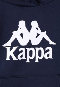 Felpa di colore blu navy con un logo grafico bianco che rappresenta due figure sedute schiena contro schiena, con il nome del marchio "Kappa" in caratteri bianchi in grassetto sottostante.