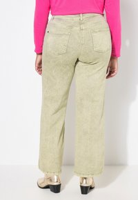 Pantalons larges vert clair avec une finition texturée, dotés de deux poches arrière et associés à des bottines à talons métalliques.