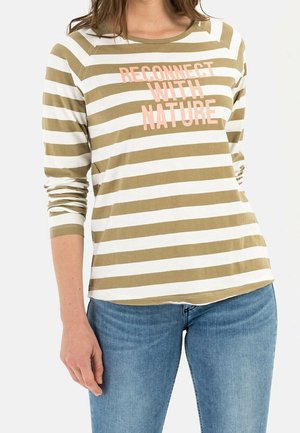 Femme portant un t-shirt à manches longues rayé olive et blanc avec le texte "RECONNECTER AVEC LA NATURE", assorti d'un jean bleu.
