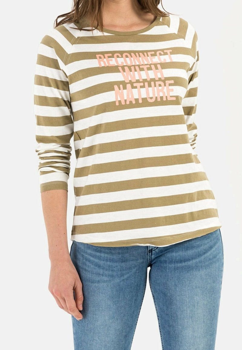 Femme portant un t-shirt à manches longues rayé olive et blanc avec le texte "RECONNECTER AVEC LA NATURE", assorti d'un jean bleu.