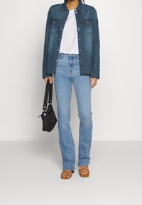 Denim jacket in dark blue with metal buttons, white t-shirt, light blue jeans, and brown strappy sandals. Black shoulder bag in hand.