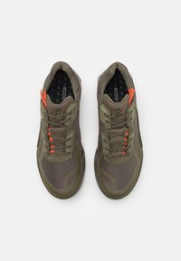 Olivgröna sportskor med ovandel i mesh, gummisula och reflekterande detaljer. Har orangea snören och vadderad krage f�ör komfort.