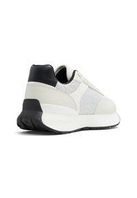 Zapatilla blanca con talón y detalles en negro, que cuenta con una parte superior de malla y paneles de cuero suave. Entresuelo grueso de espuma blanca y suela negra texturizada.