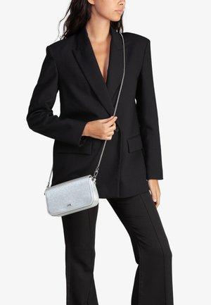 Sac à bandoulière argenté avec une texture, doté d'une anse en chaîne, associé à un blazer noir surdimensionné et un pantalon noir.