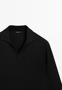 Svart pikétröja med djup V-ringning, långa ärmar och strukturerad väv. Har en subtil krage och en etikett vid halslinningen.