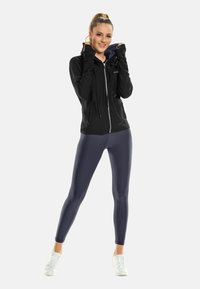 Black zip-up athletic jacket with hood, paired with high-waisted, form-fitting navy leggings and white sneakers. Smooth fabric texture.