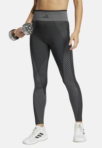 Leggings negros de cintura alta con patrones geométricos y una cinturilla texturizada, acompañados de pesas y zapatillas deportivas blancas.