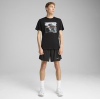 Sort bomulds t-shirt med grafisk print, parret med sorte shorts og hvide ankelstrømper. Skoene er grå med diskrete designaccenter.