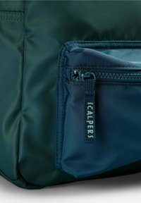 Bolsa de nylon de color verde oscuro con un bolsillo con cremallera que tiene una pestaña de cremallera azul, grabada con "SCALPERS". Textura suave con un diseño aerodinámico.