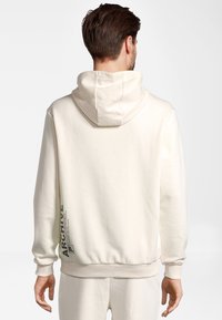 Kremowa bluza z kapturem wykonana z teksturowanej tkaniny, z prążkowymi ściągaczami na rękawach i u dołu, z pionowym nadrukiem "ARCHIVE" po boku.