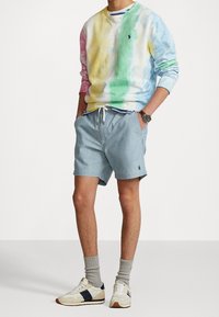 Pastellfärgad tie-dye sweatshirt med rund halsringning, matchad med ljusblå shorts som har en broderad logo, kompletterat med sneakers och strumpor.