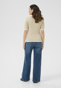 Top en tricot côtelé beige à manches courtes et bord blanc, associé à un jean bleu à jambes larges taille haute. Texture lisse, design décontracté.