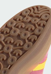 Brązowa gumowa podeszwa buta z okrągłymi i liściastymi wzorami, gładki brzeg oraz różowa cholewka z żółtymi paskami. Widoczna teksturowana powierzchnia.