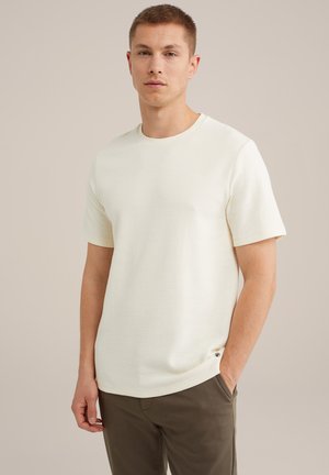 Lichtcrème t-shirt met korte mouwen, voorzien van een textuurpatroon, ronde halsuitsnijding en een klein accentlogo aan de onderrand. Gecombineerd met olijfgroene broek.
