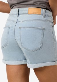 Svetlomodré džínsy na kraťasy s prehnutými okrajmi a zadnými vreckami nosené osobou v sivej košeli zasunutej dovnútra.