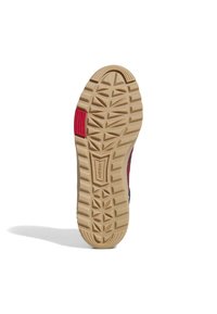 Gummisulor med en strukturerad mönstring, som har en brun botten och röda detaljer på sidan. Designen inkluderar en logotyp.