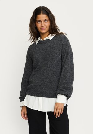 Charcoal gray knit sweater with a relaxed fit, round neck, and dropped shoulders, layered over a white collared shirt. Soft texture.