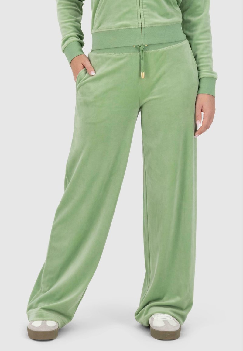 Pantalons en velours vert à coupe loose, avec une taille élastique, des poches latérales et une texture lisse. Présente des accents en métal doré.