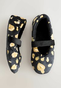 Zapatillas de terciopelo negro con un patrón amarillo y crema de diversas formas, incluyendo manos y frutas, con una correa en la parte superior.