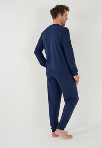 Set di abbigliamento loungewear blu navy realizzato in tessuto morbido; maglietta a maniche lunghe e pantaloni a gamba affusolata con polsini rigati; design minimalista senza motivi.