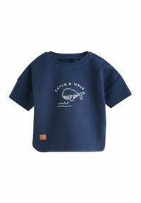 Pull léger bleu marine à manches courtes avec une texture côtelée, présentant un design brodé de baleine et de vague blanche, et une petite étiquette beige en bas.