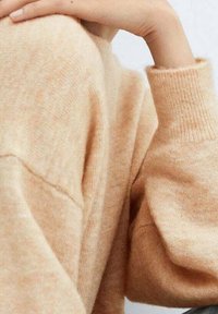 Helles Pfirsich gestricktes Sweatshirt mit lockerer Passform, gerippten Bündchen und weicher Textur. Die Details zeigen ein verschwommenes, ungleichmäßiges Muster über dem Stoff.