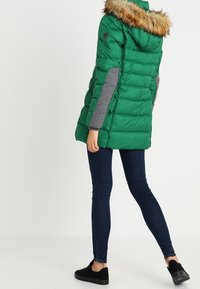 Grön puffjacka med fuskpälskantad huva, grå ärmar och quiltad textur. Matchad med mörkblå skinny jeans och svarta skor.