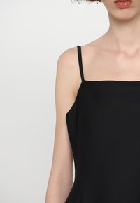 Mustmust kandevaba dress, millel on õhukesed rihmad, mis on valmistatud sileda kanga materjalist, sirge kaelusega ja voolava siluetiga.