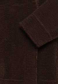 Tissu polaire texturé marron foncé montrant une manche pliée et des coutures visibles.