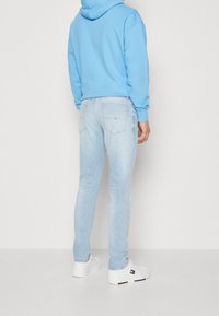 Sudadera azul clara, jeans de corte ajustado en lavado claro y zapatillas blancas. Los jeans tienen bolsillos traseros y un ligero desgastado a lo largo de las piernas.
