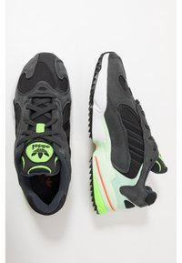 Musta ja harmaa urheilujalkine, jossa on nahka ja verkkopinta, limevihreä yksityiskohta, valkoinen välikerta ja musta tekstuuroitu pohja.