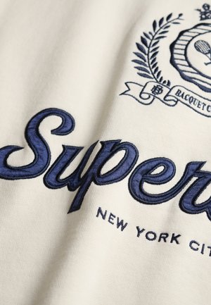 Cream fabric featuring dark blue embroidered text "Super" and "NEW YORK CITY," with decorative emblem and laurel leaf details.
