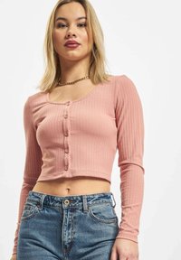 Ružičasti rebrasti dugosleeve cropped top s izrezom u obliku srca i zatvaranjem na dugmad. Nosite ga s farmerkama svijetloplave boje visokog struka.