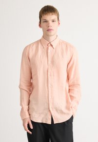 Lys rosa skjorte med knapper i en avslappet passform, laget av teksturert stoff, med en liten logo og klassisk krage, båret med svarte bukser.
