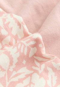 Tissu rose doux avec imprimé floral blanc, présenté en plis délicats mettant en valeur la texture et le contraste des motifs.