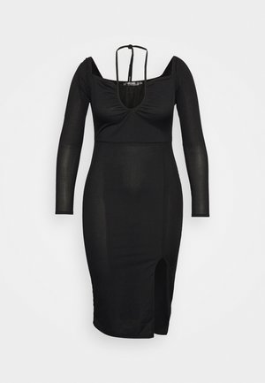 Vestido preto canelado com mangas compridas, decote em V e fenda lateral. Apresenta uma silhueta ajustada e uma fita na parte de trás do pescoço.