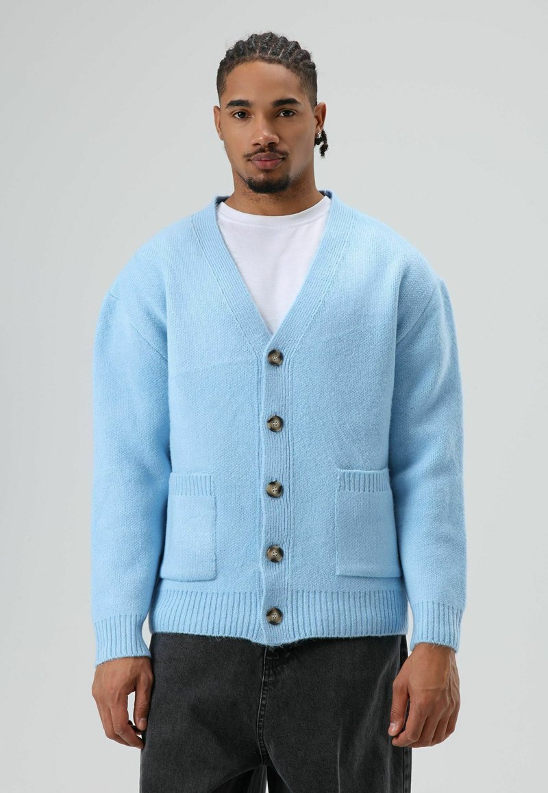 Cardigan en tricot bleu ciel avec un col en V, six boutons sur le devant, et deux poches. Comprend des poignets et un ourlet côtelés pour un effet texturé.