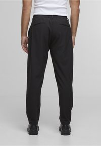 Svarte bukser med avslappet passform, med elastisk midje, to baklommer og glatt stofftekstur. Brukes med svarte sko.