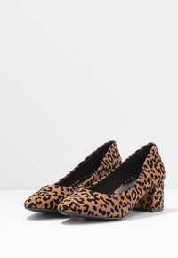 Leopard print block-heeled shoes with a pointed toe and soft suede texture. Brown base with black spots, featuring a sturdy heel design.