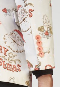 Crème jack met feestelijke Santa- en vakantie-motieven, met roze knopen op de manchetten en een gladde, gemêleerde afwerking.