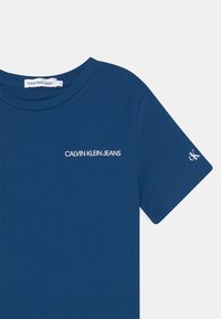 Námořnická modrá bavlněná triko s kulatým výstřihem a krátkými rukávy. Na přední straně má bílé logo "CALVIN KLEIN JEANS" a malé logo na rukávu.