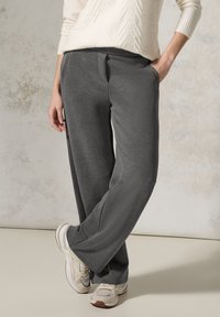 Pantalons larges gris en tissu doux et texturé, avec des poches latérales et une coupe décontractée, associés à des chaussures de sport beiges.