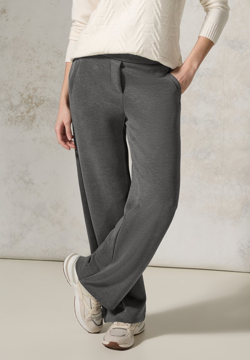 Pantalons larges gris en tissu doux et texturé, avec des poches latérales et une coupe décontractée, associés à des chaussures de sport beiges.