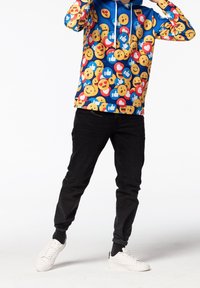 Sudadera con capucha con fondo azul cubierto de varios patrones de emojis, combinada con jeans negros y zapatillas blancas.