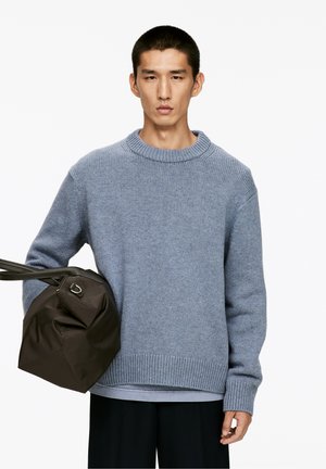 Helles blaues Strickpullover mit einem gerippten Rundhalsausschnitt und Ärmeln, kombiniert mit einer braunen übergroßen Tasche mit stabilen Griff.