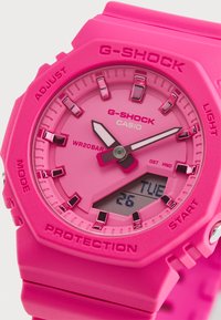 G-SHOCK pulkstenis ar spilgti rozā sveķu korpusu, atbilstošu joslu, analogo-digitālo displeju un sīkām stundu atzīmēm. Ūdensizturīgs līdz 20 bāriem.