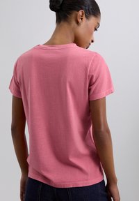 T-shirt en coton rose à manches courtes avec une coupe décontractée. Il présente un col rond simple et une texture lisse, sans motifs ni accents visibles.