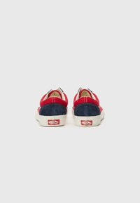 Red and navy canvas sneakers with a rubber sole, featuring a classic low-top design and white stitching accents at the back.
