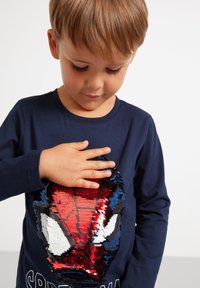 Marineblaue Langarmbluse mit einem wendbaren Pailletten-Design eines Spiderman-Gesichts in Rot, Weiß und Blau, mit weichem Material.